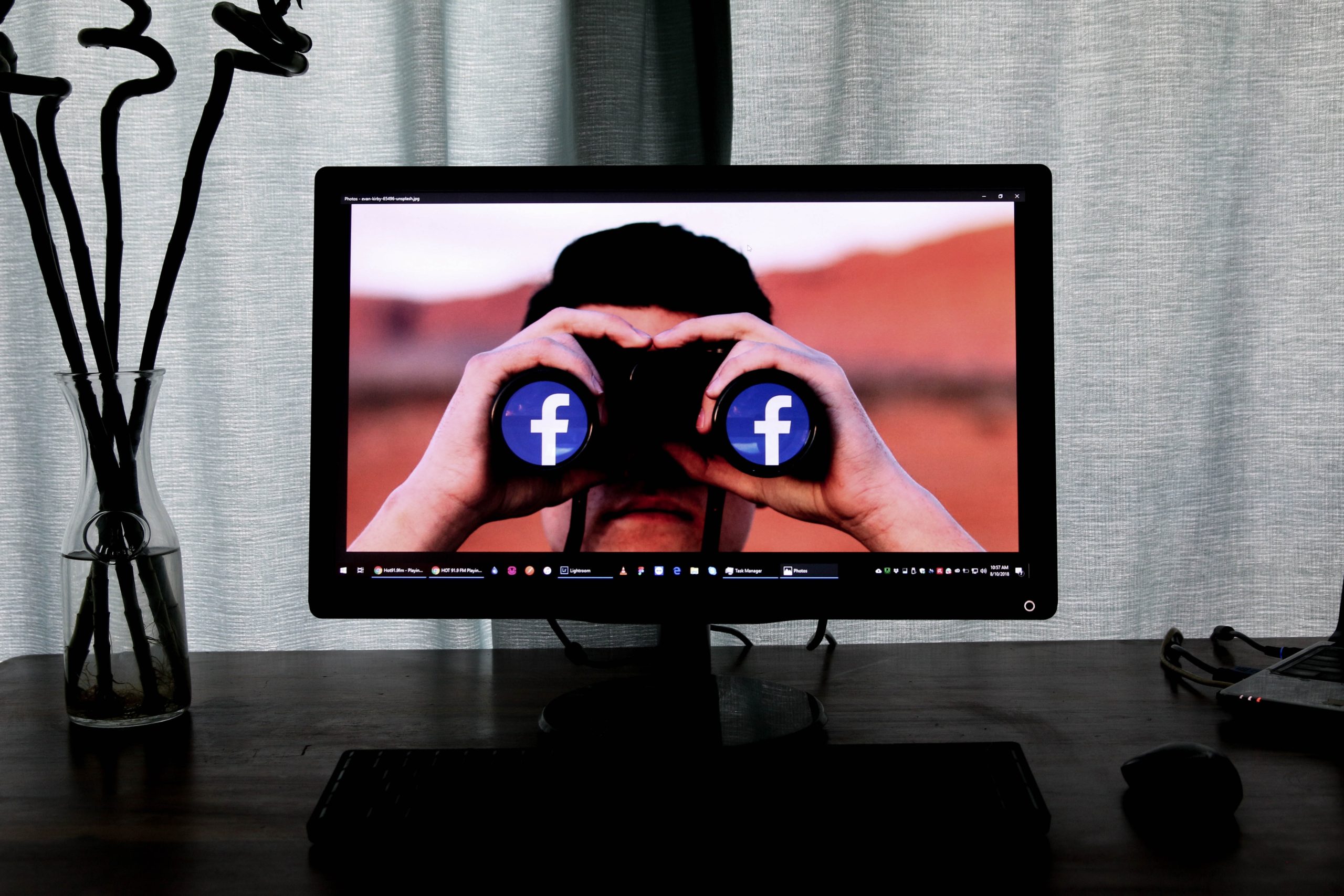 A TV screen shows a person holding binoculars with Facebook logos